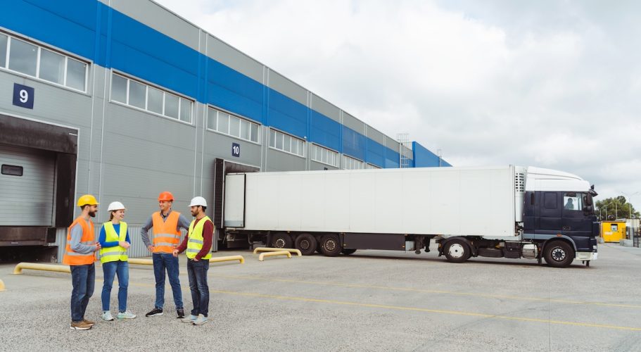 Successful workers, managers, engineers in hard hats standing on the street near cargo terminal Group of successful workers, managers, engineers in hard hats standing on the street near cargo terminal, copy space, mockup, talking. Concept of transportation, business