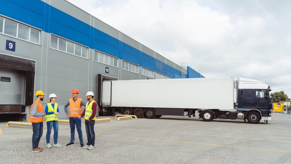 Successful workers, managers, engineers in hard hats standing on the street near cargo terminal Group of successful workers, managers, engineers in hard hats standing on the street near cargo terminal, copy space, mockup, talking. Concept of transportation, business