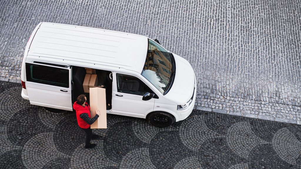 An aerial view of delivery man courier with face mask delivering parcel box in town.